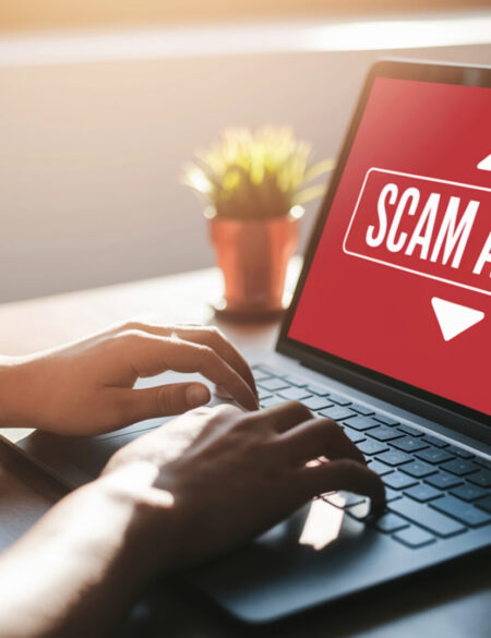 Person using laptop displaying a scam alert warning on screen, signifying digital safety awareness.