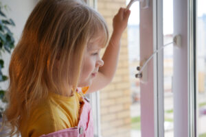 A young girl tries to open the window standing on the windowsill on a high floor.