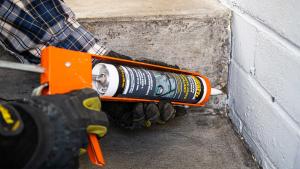 Gloved hand applying Quikrete Advanced Polymer Concrete Crack Sealant with caulking gun