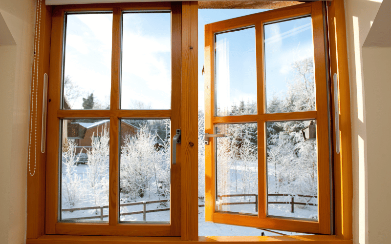 Wood-framed casement windows opening to a snowy landscape